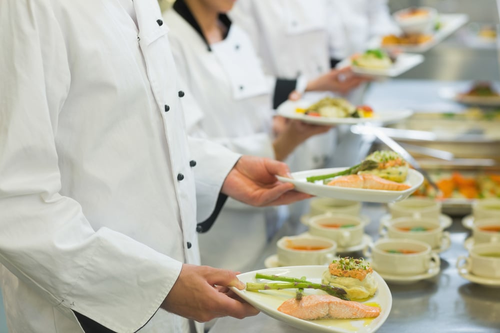 Chef holding salmon dishes standing in a row with colleagues