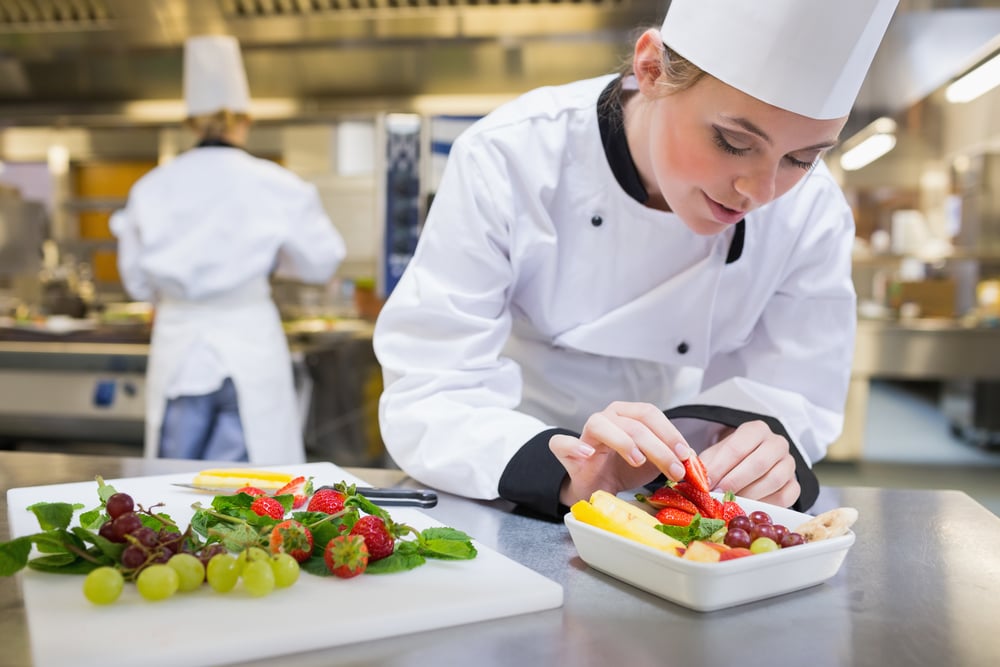 Chef putting a strawberry in a fruit salad in the kitchen