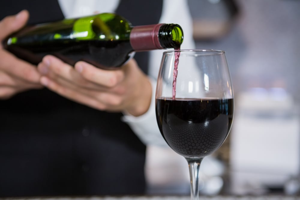 Bartender pouring red wine into a glass on a bar counter