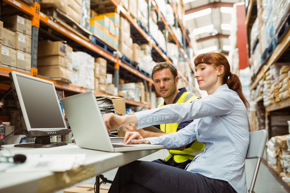 Warehouse worker and FM Manager looking at laptop in a large warehouse